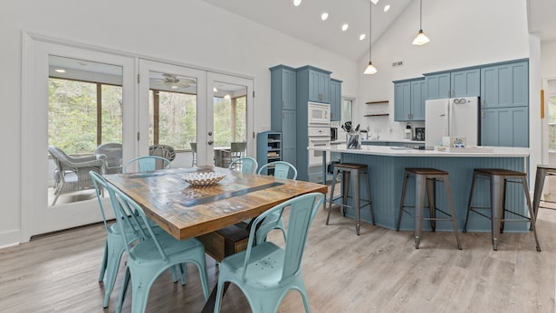 A spacious kitchen with blue cabinets, a wooden dining table, and light-colored flooring. - Beautiful Sound Side Home w/Private Beach Access (Hawthorne Haven) (Pine Knoll Shores)