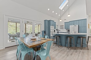 Een ruime keuken met blauwe kastjes, een houten eettafel en lichtgekleurde vloeren.