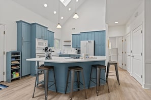 Een moderne keuken met blauwe kastjes, een centraal eiland met krukken, een magnetron en een koelkast.