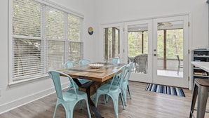 A dining area with a wooden table and turquoise chairs, large windows with blinds, and a view of the outdoors. - Beautiful Sound Side Home w/Private Beach Access (Hawthorne Haven) (Pine Knoll Shores)