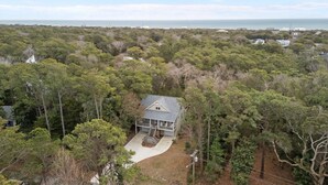 A house surrounded by dense forest with a clear view of the ocean in the background. - Beautiful Sound Side Home w/Private Beach Access (Hawthorne Haven) (Pine Knoll Shores)