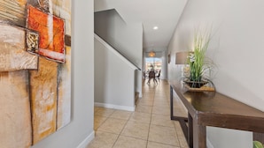 A hallway with a staircase, a dining area in the background, and a potted plant on a console table. - 8847 Candy Palm Road (Kissimmee)