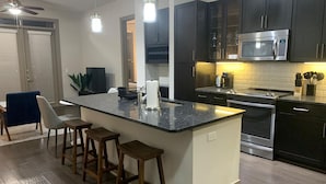 A modern kitchen with dark cabinets, a stainless steel microwave, and a large island with bar stools. - Relax at Cityline I Premium 2BR in Dallas (Plano)