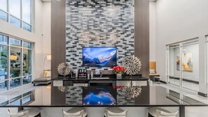 A modern kitchen with a large island, bar stools, and a flat-screen TV mounted on a textured wall. - Relax at Cityline I Premium 2BR in Dallas (Plano)