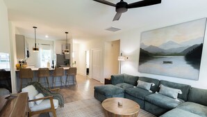 A modern living room with a sectional sofa, a coffee table, and a painting of a lake. - Upscale Lodge Sleeps 9 Dog Friendly Near CU (Central)
