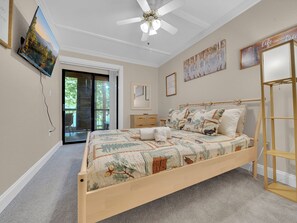 A bedroom with a large bed, a ceiling fan, a television mounted on the wall, and a sliding glass door leading to an outdoor area.
