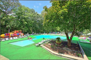 A swimming pool with a water slide, surrounded by lounge chairs and a tree.