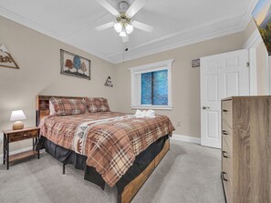 Ein Schlafzimmer mit Bett, Nachttisch, Lampe, Deckenventilator, Fenster mit blauen Vorhängen und einem Kleiderschrank.