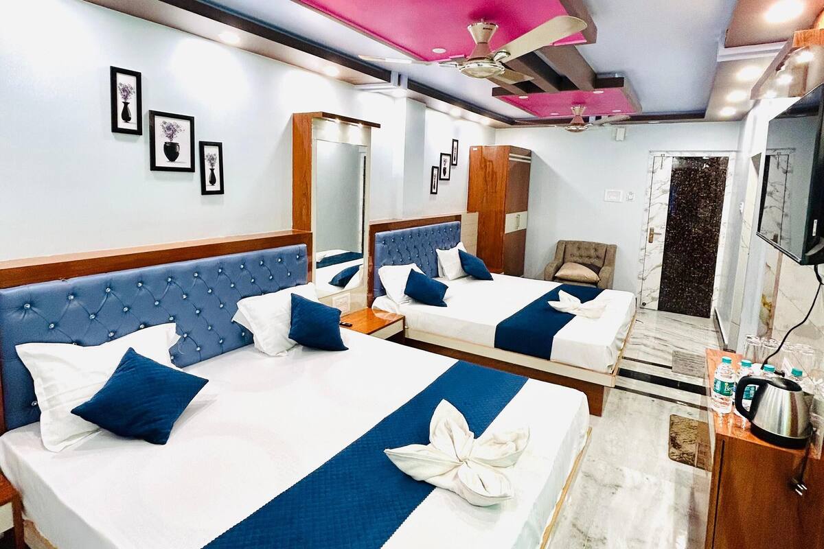 A hotel room with two beds, a ceiling fan, a mirror, and a TV.