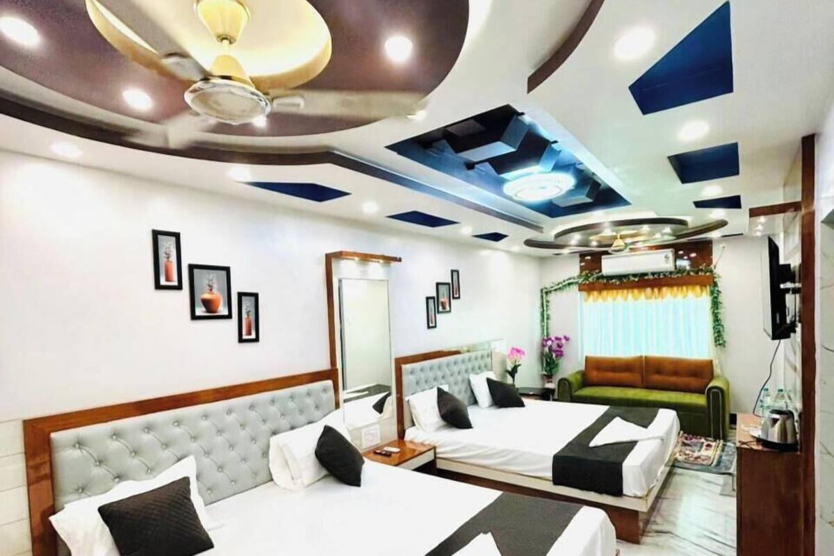 A hotel room with two beds, a large mirror, a sofa, and a TV.
