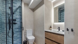A modern bathroom with a glass shower enclosure, a toilet, and a vanity with a mirror. - Waou Malasaña VII - Short Term Rental (Madrid)