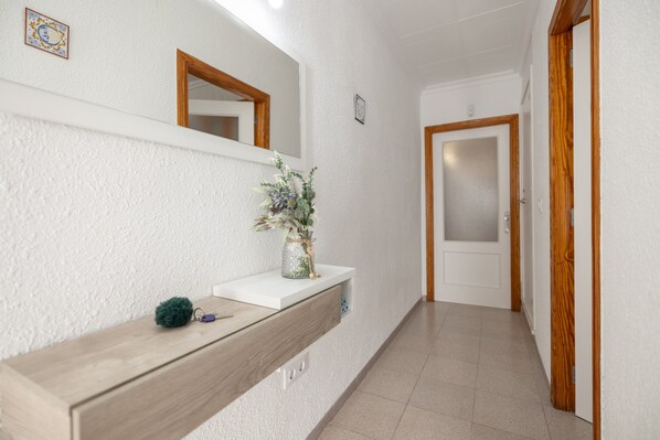 A hallway with a wooden bench, a white wall, a mirror, and a door.