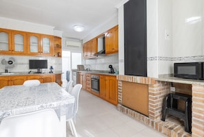 Una cocina con armarios de madera, horno empotrado, microondas y una zona de comedor con mesa y sillas.