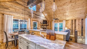 L’intérieur d’un chalet en bois comprend une cuisine, un coin repas et une cheminée en pierre.
