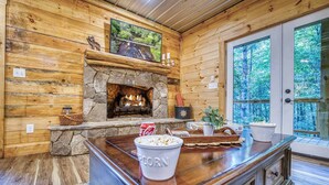 L’intérieur d’une cabane en rondins, avec une cheminée en pierre, des murs en bois, une grande fenêtre et un coin bar où l’on peut prendre des en-cas.