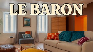 Ein modernes Wohnzimmer mit Sofa, Sessel, Hocker und einem gemusterten Teppich.