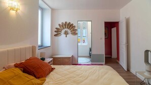 Ein Schlafzimmer mit Bett, Nachttisch, Lampe, Spiegel und Fenster.