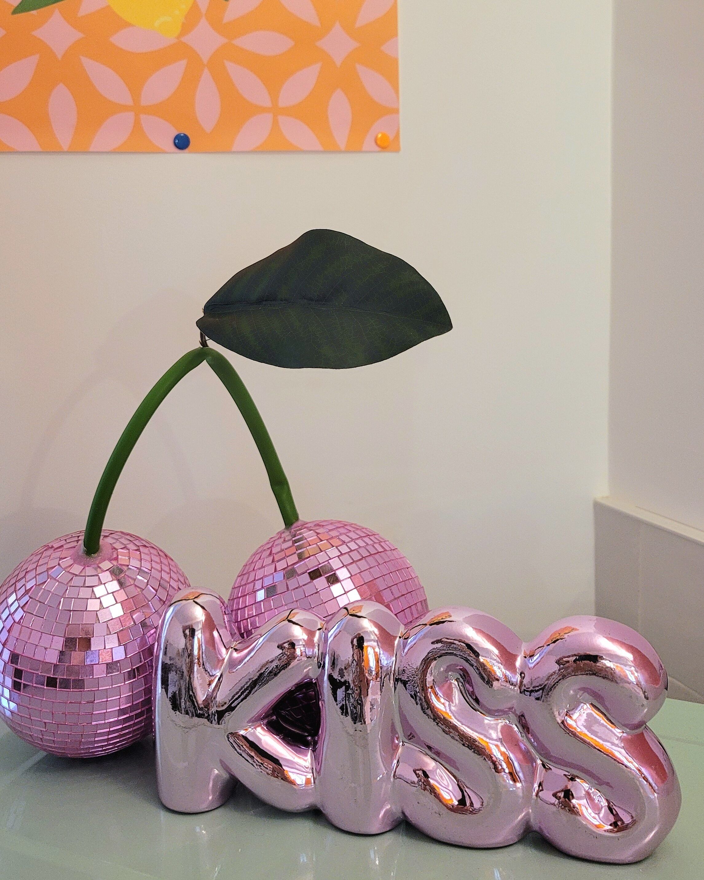 Eine dekorative Anordnung mit einer Discokugel und einem herzförmigen Gegenstand mit dem Schriftzug 'KISS' auf einer Tischplatte.