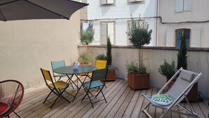 Eine Holzterrasse mit Tisch und Stühlen, Blumentöpfen und einer Sonnenliege.