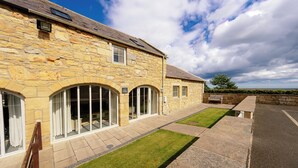 A stone building with large windows and a paved patio area. - 
A beautifully restored cottage, sitting on the stunning Northumbrian coastline. (Warkworth)