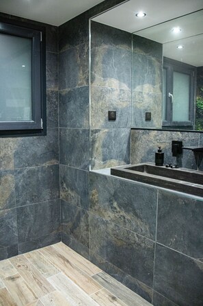 Un baño moderno con baldosas de piedra oscura, un espejo grande y suelo de madera.