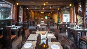A restaurant with multiple dining tables and chairs, wooden ceiling beams, and hanging light fixtures. - Badi Garh Resort (Udaipur)