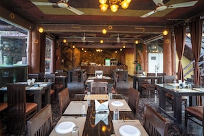 A restaurant with multiple dining tables and chairs, wooden ceiling beams, and hanging light fixtures. - Badi Garh Resort (Udaipur)