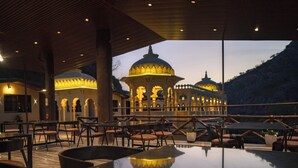 An outdoor dining area with tables and chairs, a reflective pool, and a building with domed architecture in the background. - Badi Garh Resort (Udaipur)