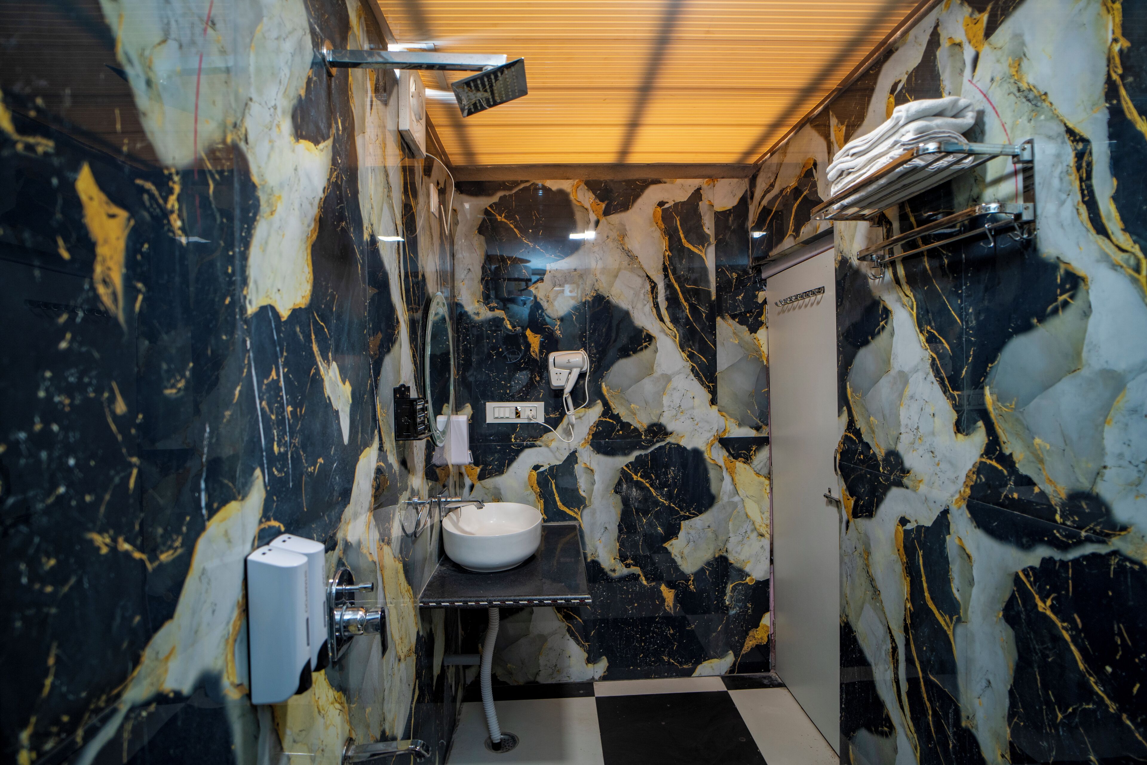 A bathroom with a marble wall, a sink, a towel rack, and a shower head.