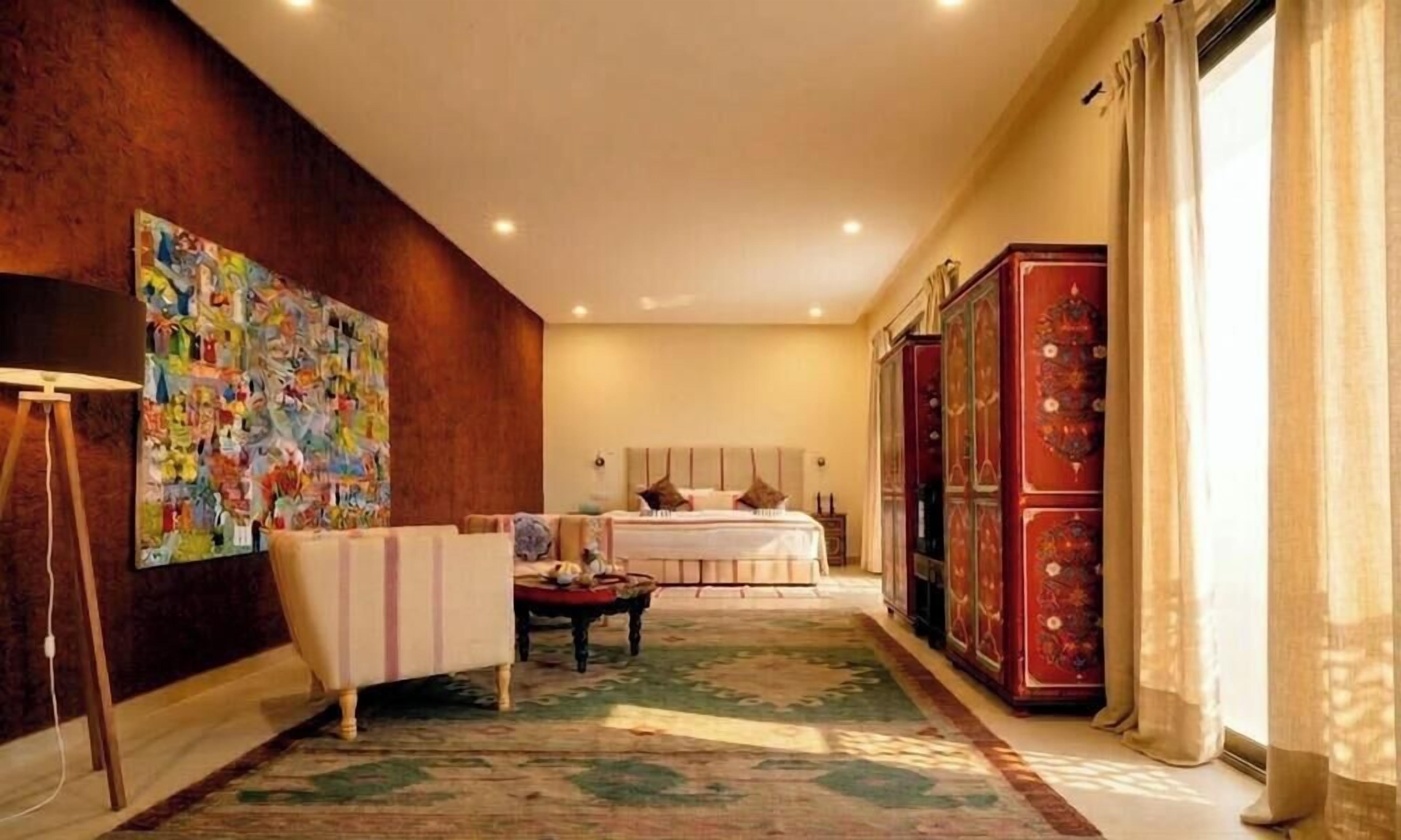 A hotel room with a bed, a desk, a chair, a large painting, and a wardrobe.