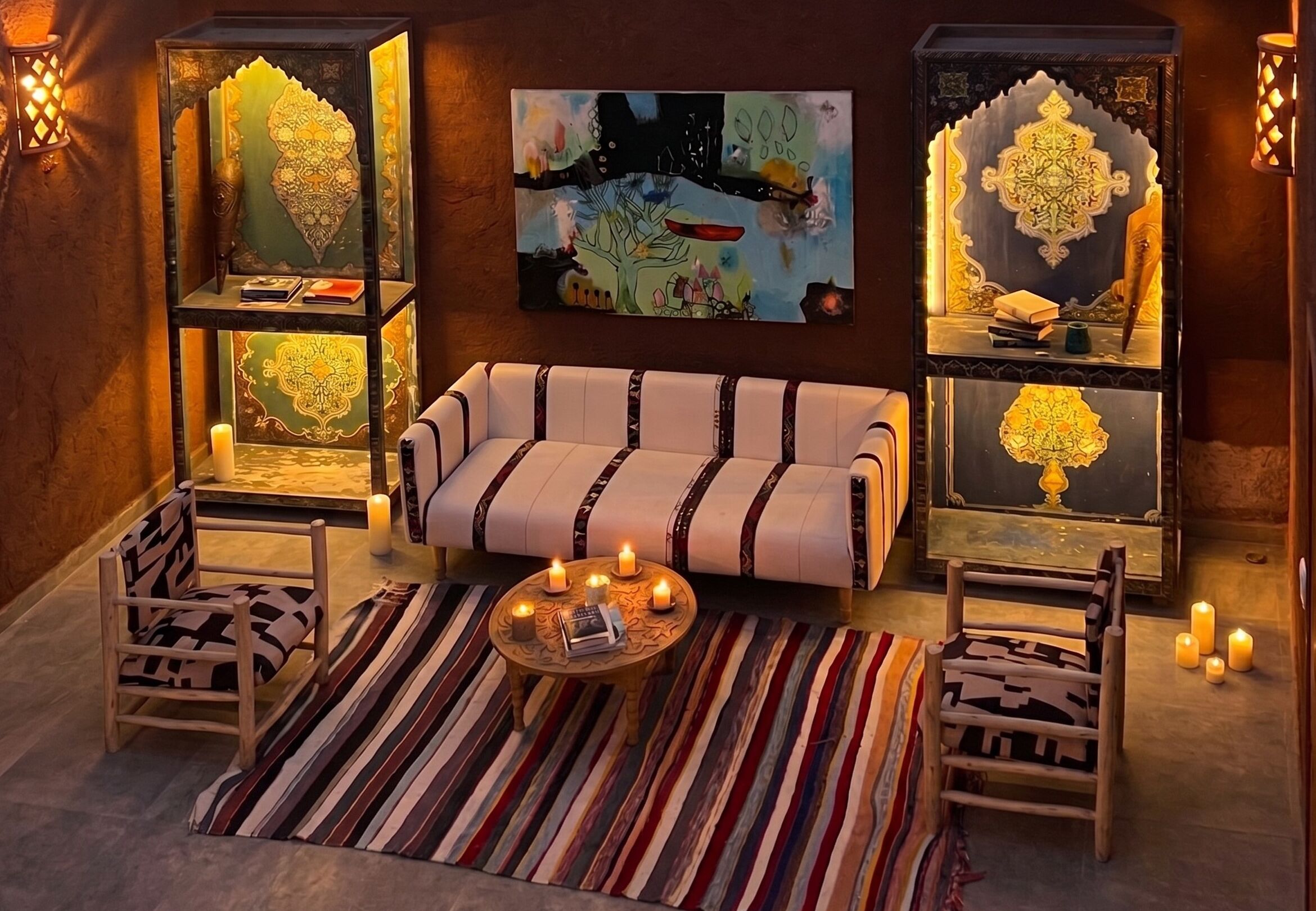A cozy room with a sofa, patterned chairs, a coffee table with candles, and decorative shelves with illuminated objects.