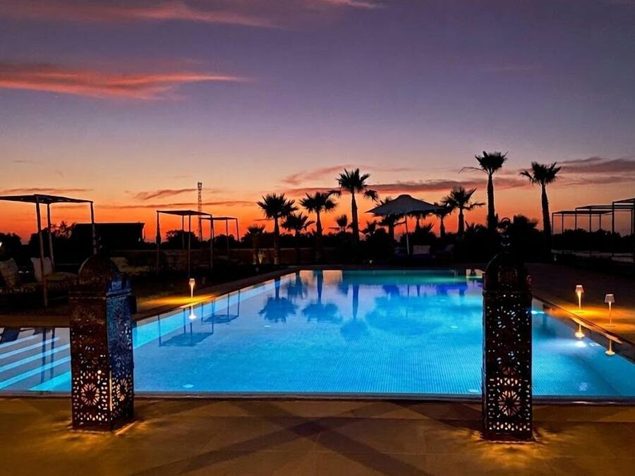 Una piscina al atardecer con palmeras y un ocaso en el fondo.