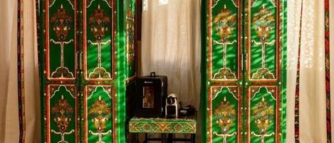 Two ornate green cabinets with intricate designs, a small table with a patterned cloth, and a black object on the table.