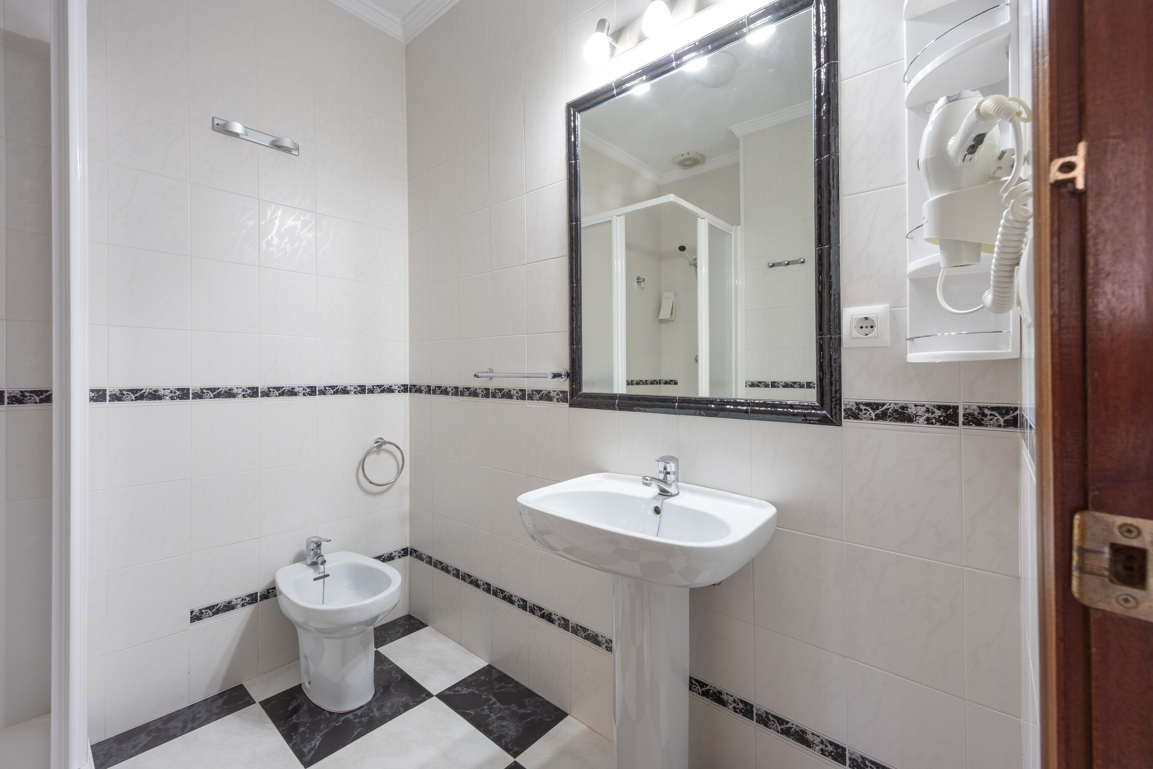 A bathroom with a bidet, a sink, a mirror, and a shower area.