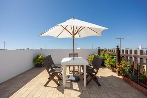 A patio with a table and chairs, an umbrella, and potted plants.