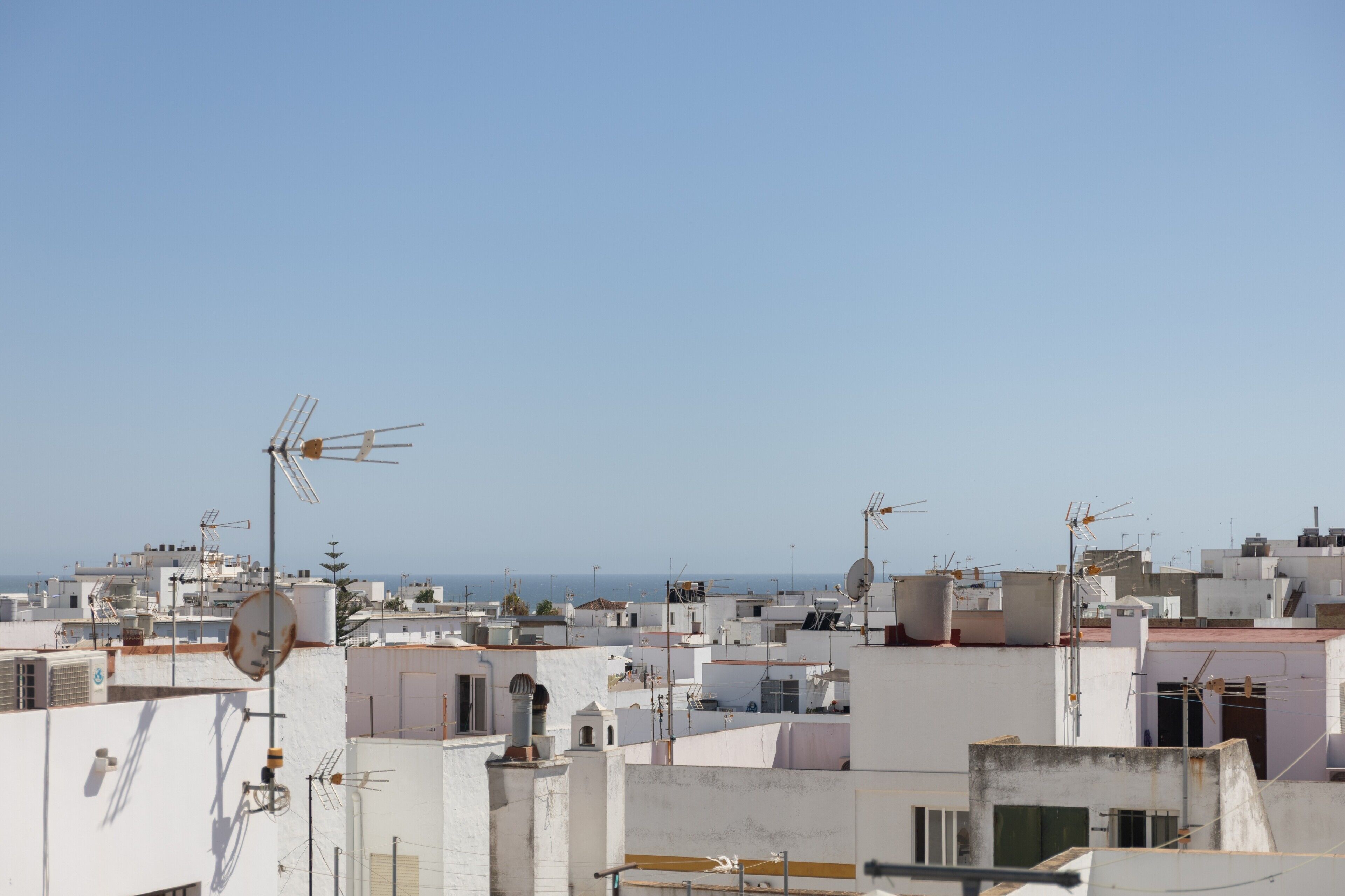 A densely packed urban area with multiple buildings, some with satellite dishes and antennas, under a clear sky.