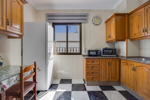 A kitchen with wooden cabinets, a refrigerator, a microwave, and a window with a balcony view.