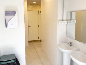 A bathroom with a hand dryer, a sink, a mirror, and a trash bin. - Nomada Hostel El Palmar de Vejer (Vejer de la Frontera)