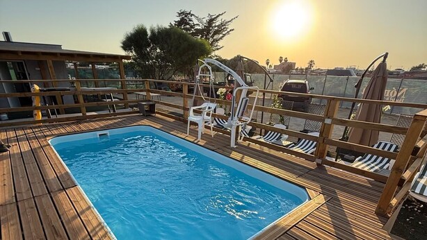 Una terraza de madera con una piscina rectangular, sillas de descanso y un parasol.