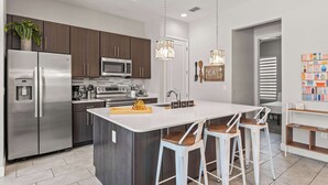 A modern kitchen with stainless steel appliances, a large island with bar stools, and pendant lighting.