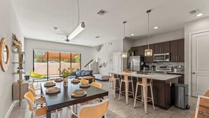 A modern kitchen with a central island, bar stools, and a dining area with a long table and chairs.