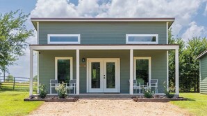 A two-story building with a covered front porch, two windows on the upper floor, and a door with glass panels. - Countryside Escape | 5 minutes to Round Top | 2BR (Round Top)