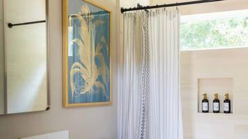 Une salle de bain avec un meuble-lavabo blanc, une œuvre d’art encadrée, un rideau de douche et des articles de toilette rangés sur une étagère.