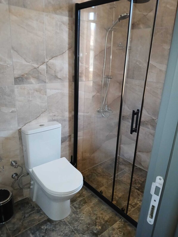 Un baño con inodoro, ducha con mampara de vidrio y paredes de azulejos.