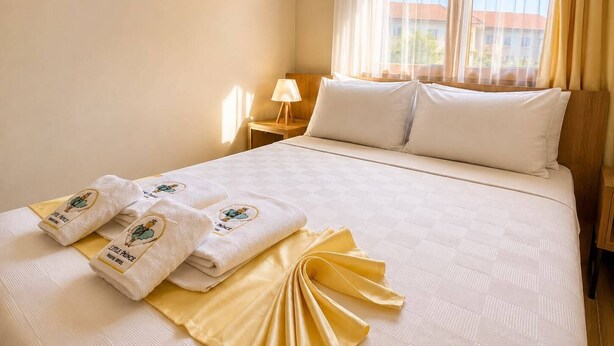 Una habitación de hotel con cama, almohadas, una mesita de noche con lámpara y una ventana con cortinas.