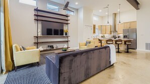 A modern living room with a sofa, chairs, a TV, and a kitchen in the background. - East Austin Modern | Rooftop Deck | Walk to Bars (Austin)