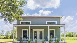 A two-story house with a covered porch and a small garden area. - Hidden Gem Near Round Top | 2BR Cottage (Round Top)