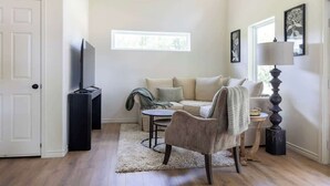 A living room with a sofa, armchair, TV stand, and a window. - Hidden Gem Near Round Top | 2BR Cottage (Round Top)