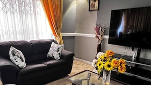 A modern living room with a dark sofa, patterned cushions, a glass coffee table, and a vase with flowers.