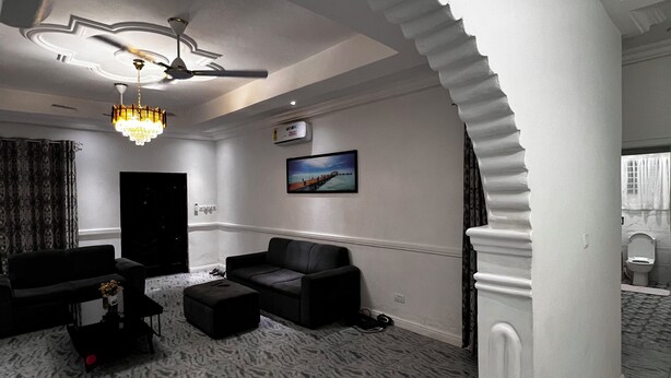 A living room with a patterned carpet, a black sofa, a coffee table, a chandelier, and a ceiling fan.